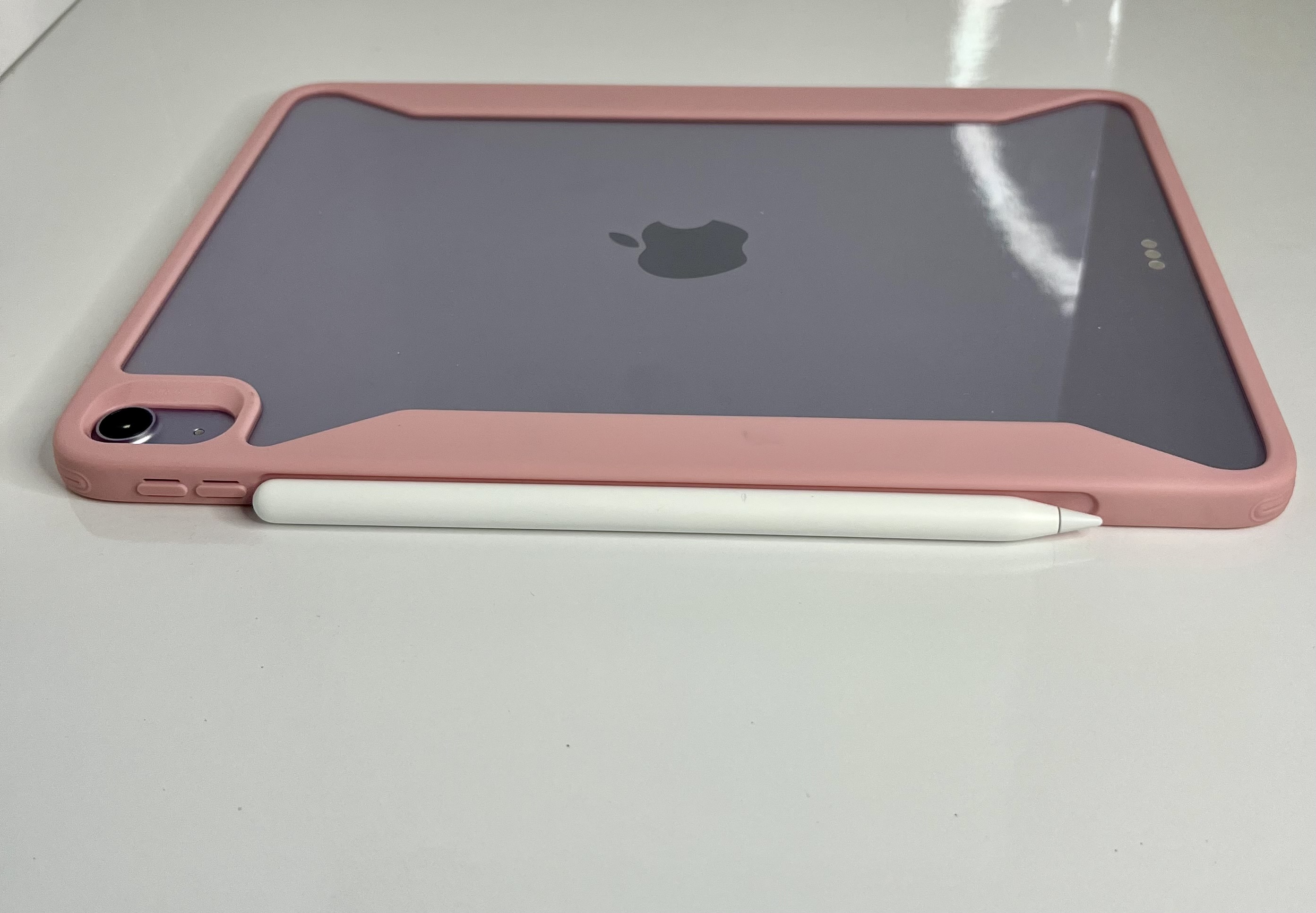 The back of an iPad with a pink case is displayed flat, featuring the Apple logo and attached stylus.