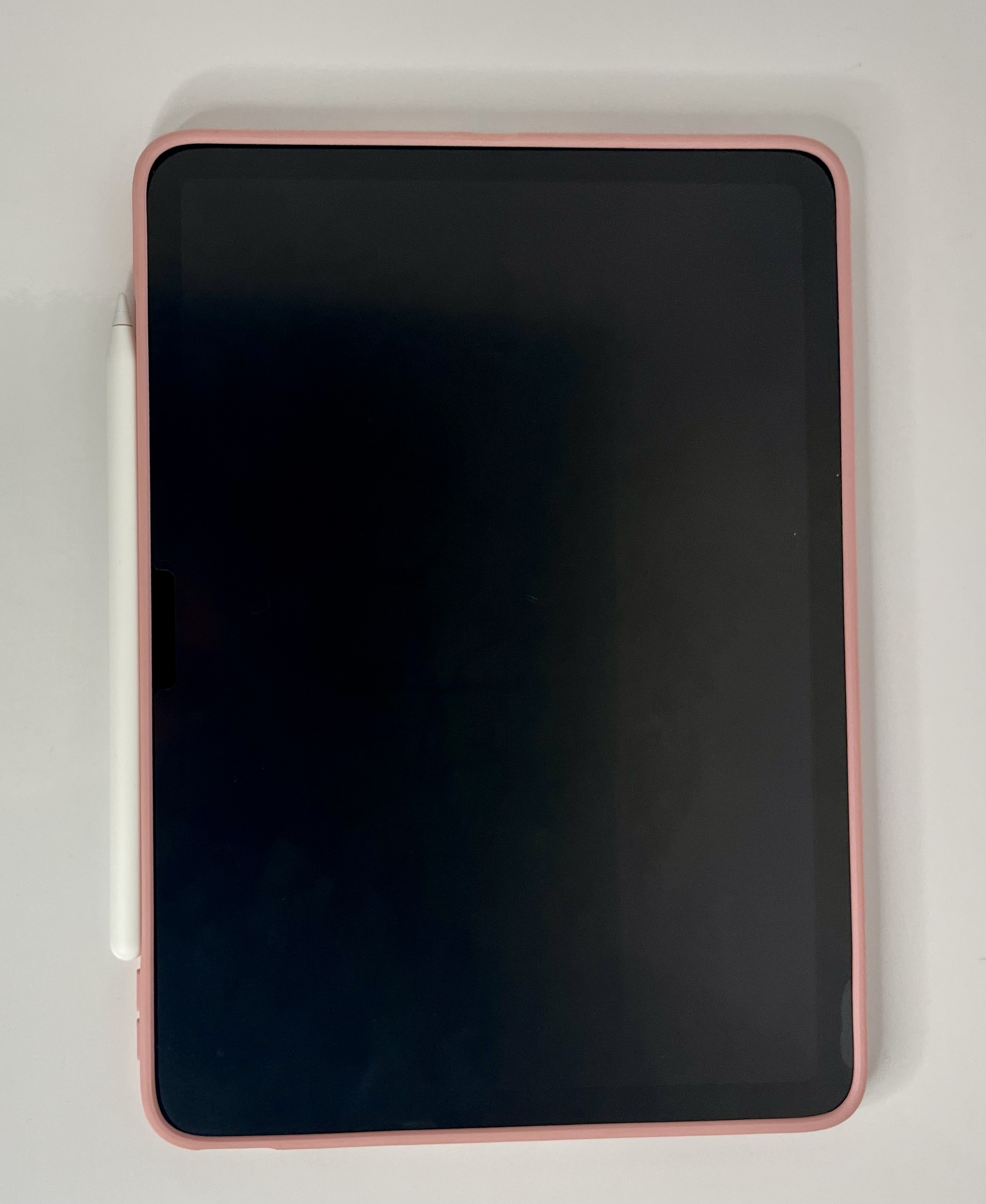 An iPad with a pink case and attached stylus is shown from above, its dark screen filling the frame.