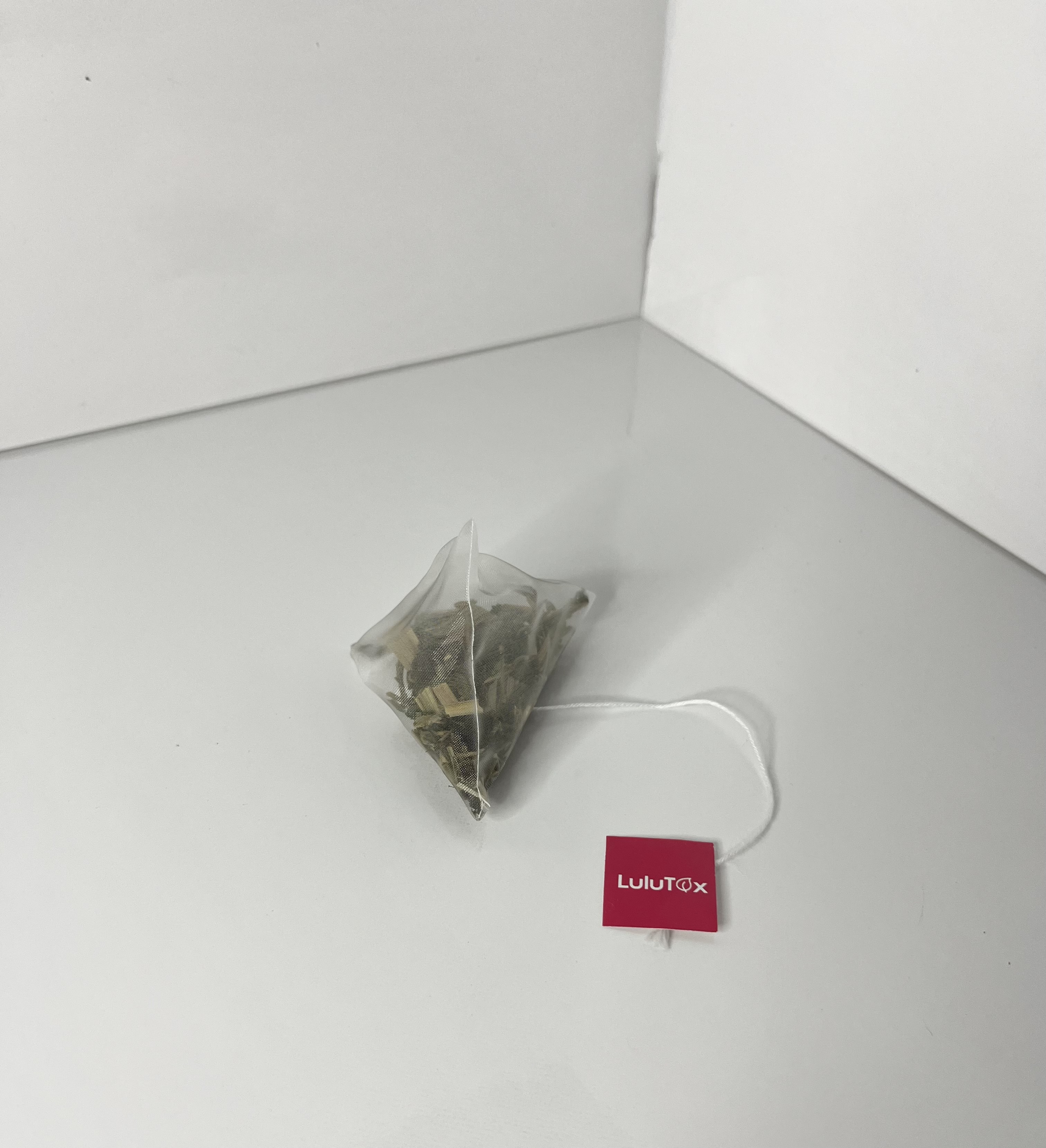 A pyramid-shaped LuLuTox tea bag with a string and red label sits upright on a white surface.