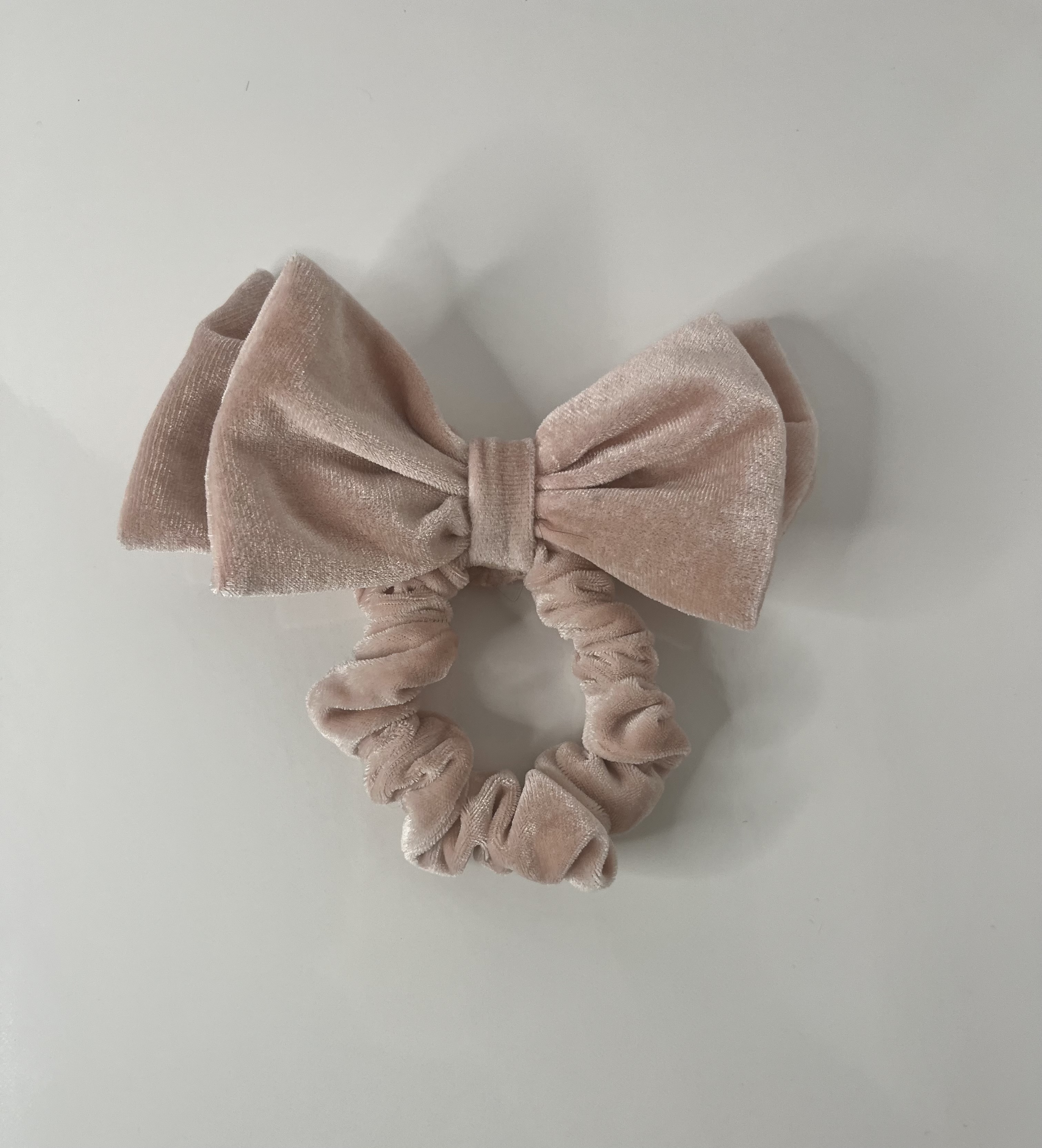 The scrunchie is positioned against a white background, its gathered fabric and bow seen from a slightly different perspective.
