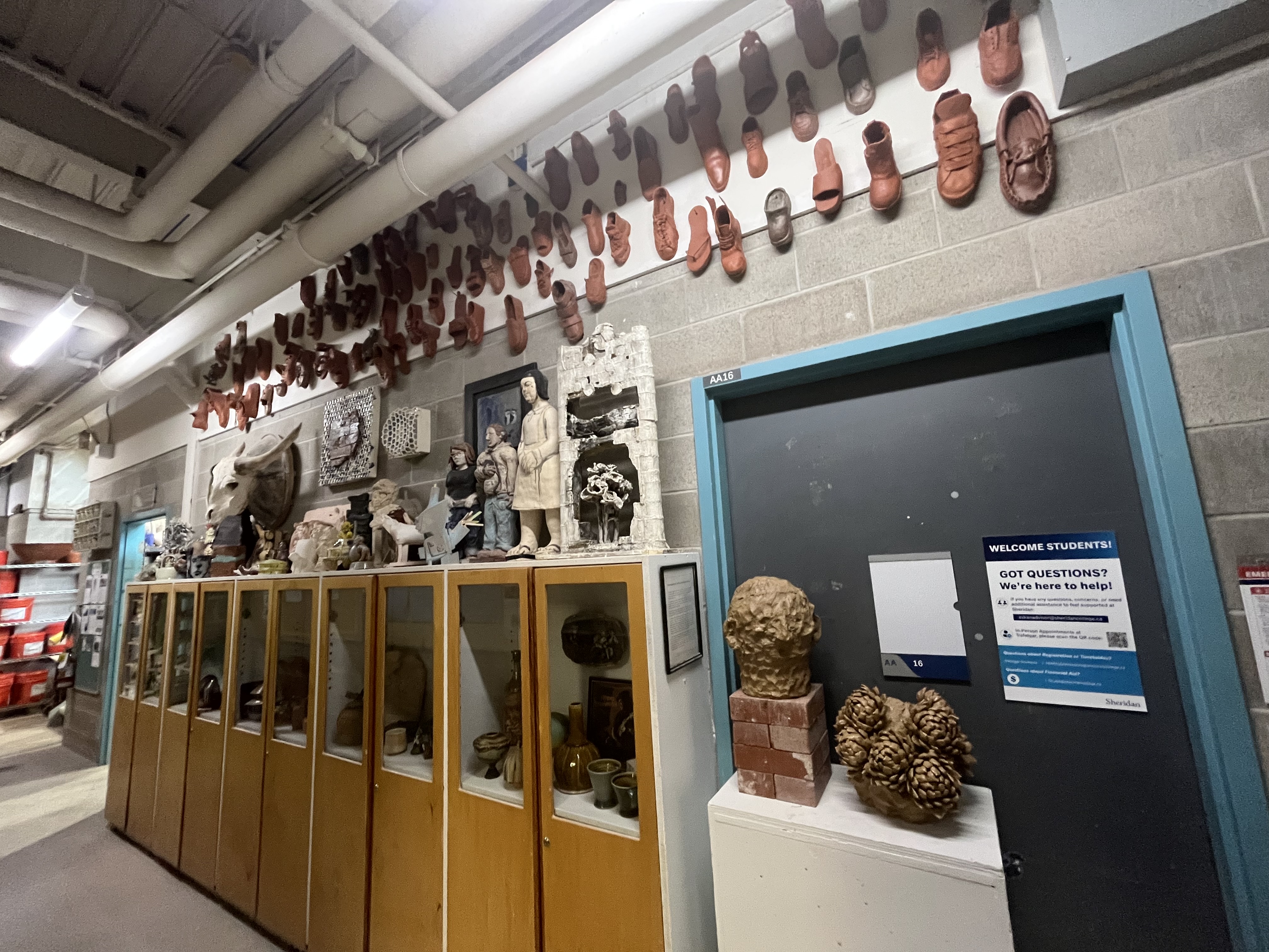 Ceramic masks, sculptural works, and archived student projects line the hallway, creating a curated gallery atmosphere within the workspace.