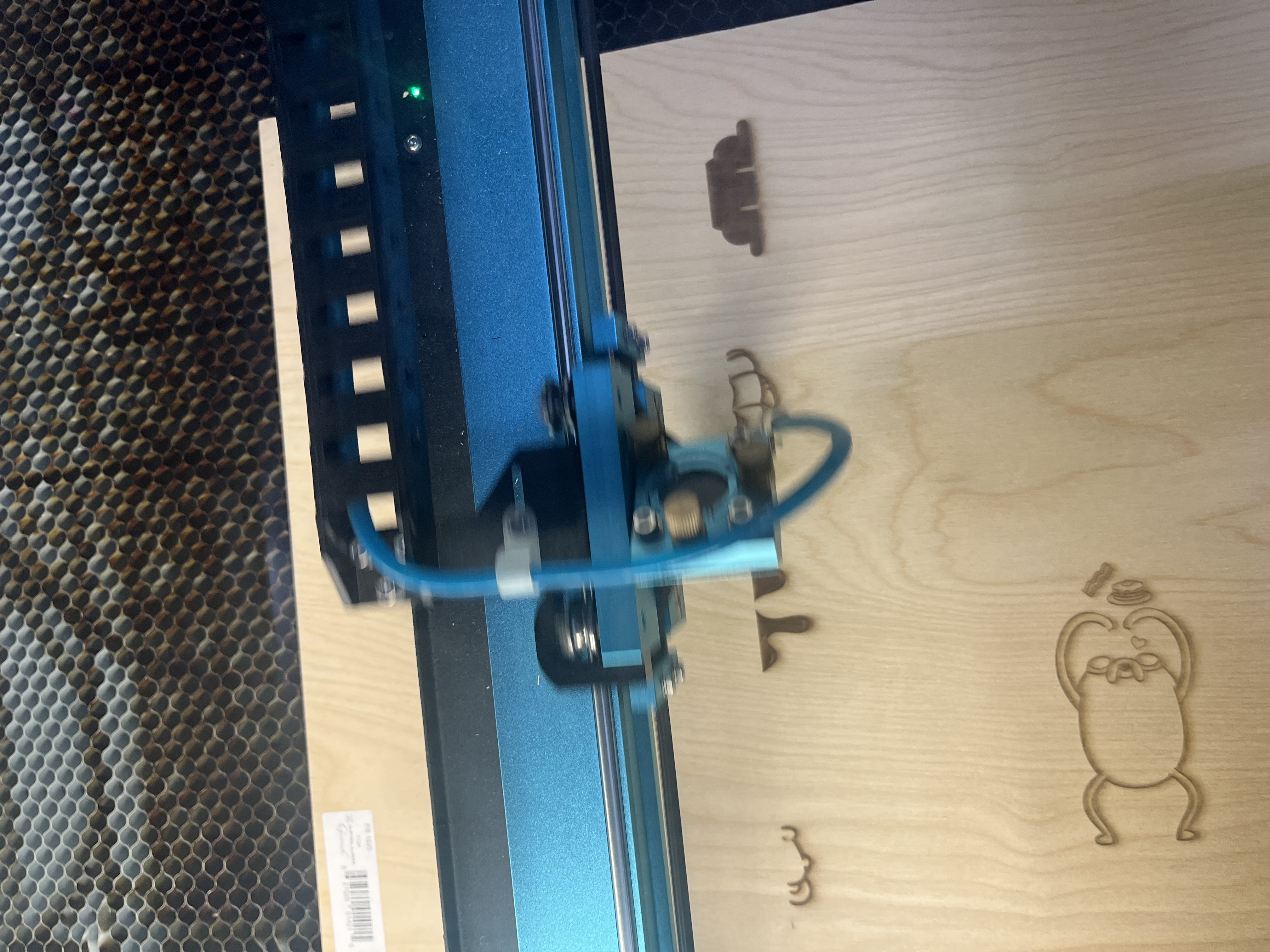 Four individual laser-cut plywood phone-stand components are displayed, including two structural base pieces and two engraved decorative panels featuring illustrated characters.